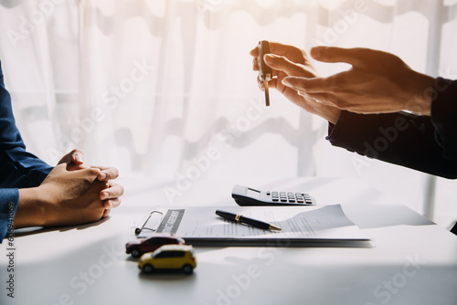 Man signing car insurance document or lease paper. Writing signature on contract or agreement. Buying or selling new or used vehicle. Car keys on table. Warranty or guarantee. Customer or salesman. photo