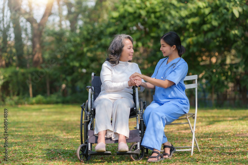 Asian nurse or physiotherapist caring for elderly woman sitting wheelchair. Asian female nurse takes care of patients and takes them for a walk in the hospital park.