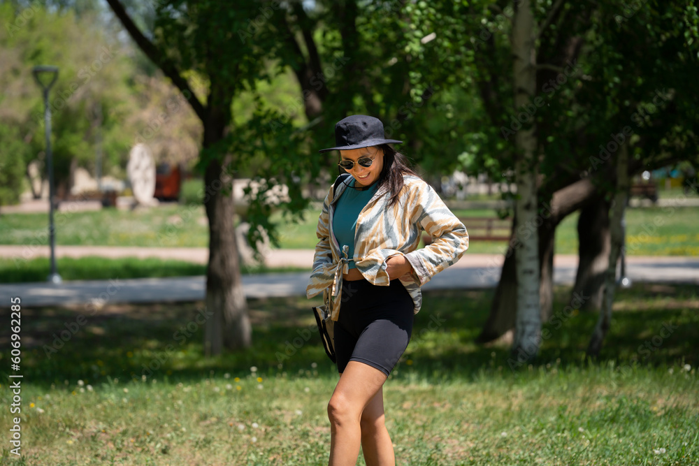 The general plan of a young woman, Asian (Kazakh) in sunglasses and a hat. A happy girl walks in a summer park.