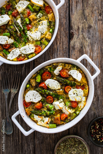 Bread casserole with green asparagus, goat cheese, tomatoes and eggs on wooden table 