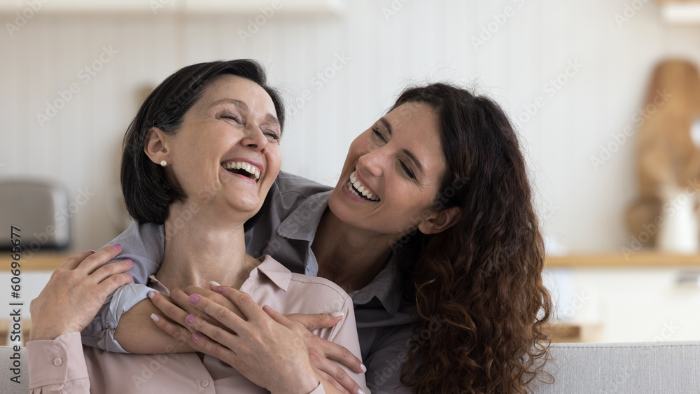 Cheerful daughter woman hugging happy excited mature mom with love, gratitude, joy, celebrating mothers day, laughing out loud, having fun. Mother and adult kid casual home portrait Cheerful daughter woman hugging happy excited mature mom with love, gratitude, joy, celebrating mothers day, laughing out loud, having fun. Mother and adult kid casual home portrait