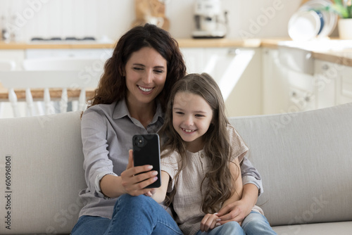 Happy beautiful mother and pretty little daughter girl using online learning application on smartphone for preschooler education, talking on video call, enjoying internet communication