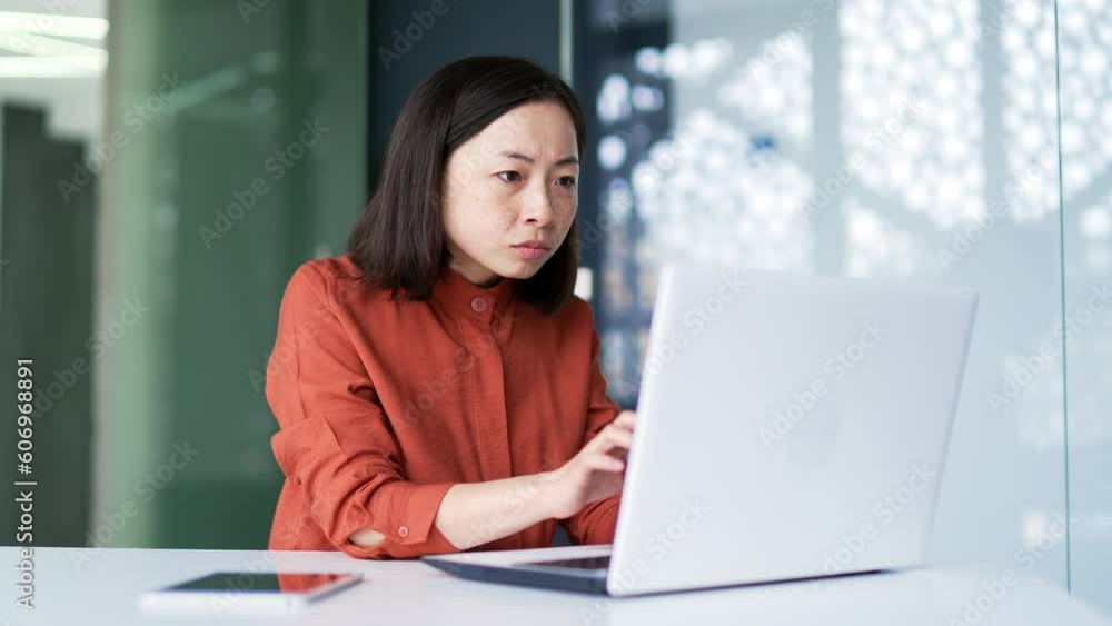 Frustrated Asian woman complaining about poor performance of computer program on laptop while sitting in modern office. Businesswoman is dissatisfied with the work of a computer, Internet or service Frustrated Asian woman complaining about poor performance of computer program on laptop while sitting in modern office. Businesswoman is dissatisfied with the work of a computer, Internet or service
