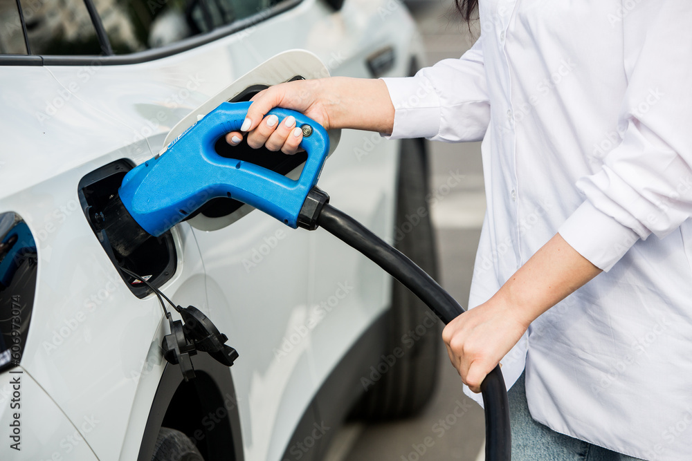 Young business woman refueling her electric car at a EV charging station. Concept of environmentally friendly vehicle. Electric car concept. Green travelling. Young business woman refueling her electric car at a EV charging station. Concept of environmentally friendly vehicle. Electric car concept. Green travelling.