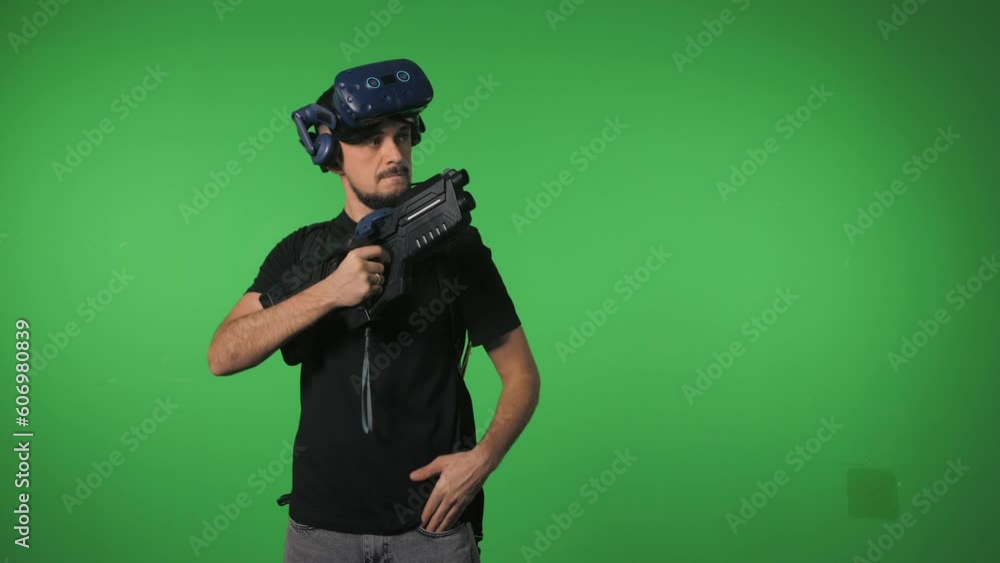 Portrait of a man on a green background in virtual reality gaming equipment with a gaming automatic rifle in his hands. Portrait of a man on a green background in virtual reality gaming equipment with a gaming automatic rifle in his hands.