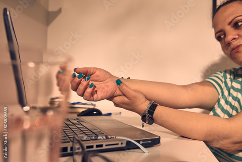 Woman with hand pain while working on a laptop at home.
