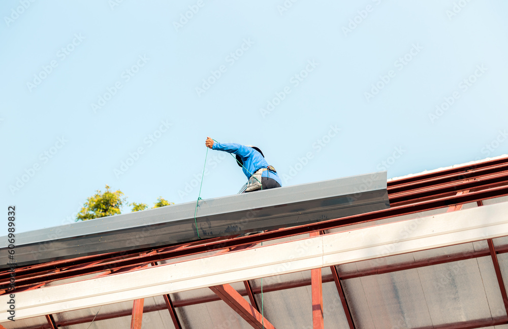 Roofer working in special protective work wear gloves, using air or pneumatic nail gun installing asphalt shingle on top of the new roof, Concept of residential building under construction.