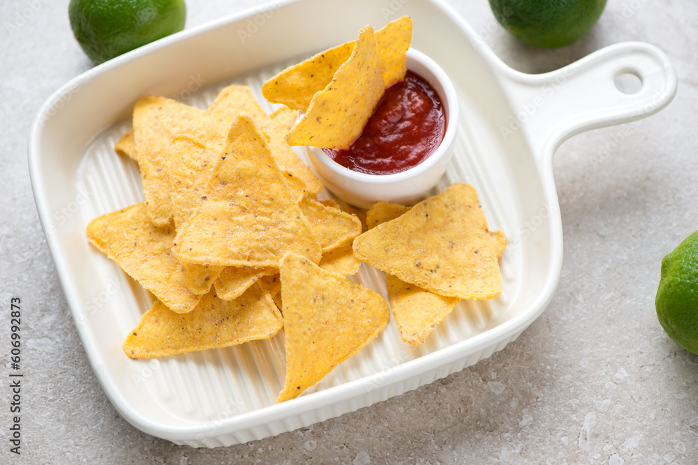 Mexican nachos chips with dip in a light-beige serving pan, horizontal shot on a beige stone background, selective focus Mexican nachos chips with dip in a light-beige serving pan, horizontal shot on a beige stone background, selective focus