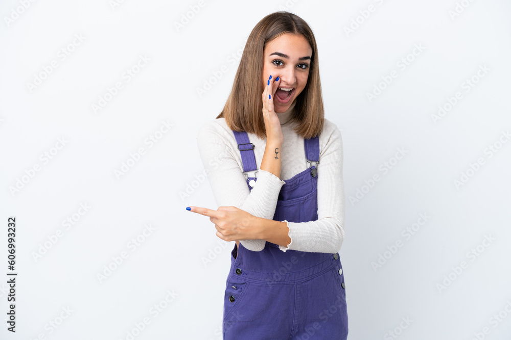 Young caucasian woman isolated on white background pointing to the side to present a product and whispering something Young caucasian woman isolated on white background pointing to the side to present a product and whispering something