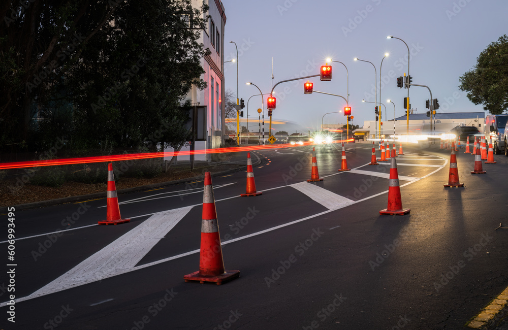 Orange traffic cones lined up on the road. Car light trails on the road intersection. Auckland.