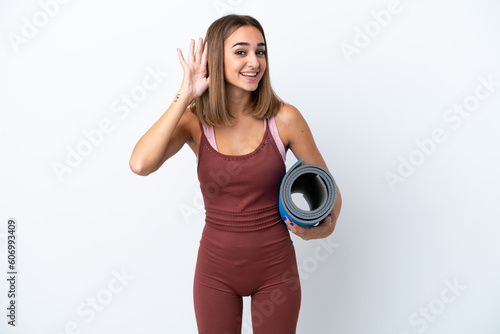 Young sport caucasian woman going to yoga classes isolated on white background listening to something by putting hand on the ear © luismolinero