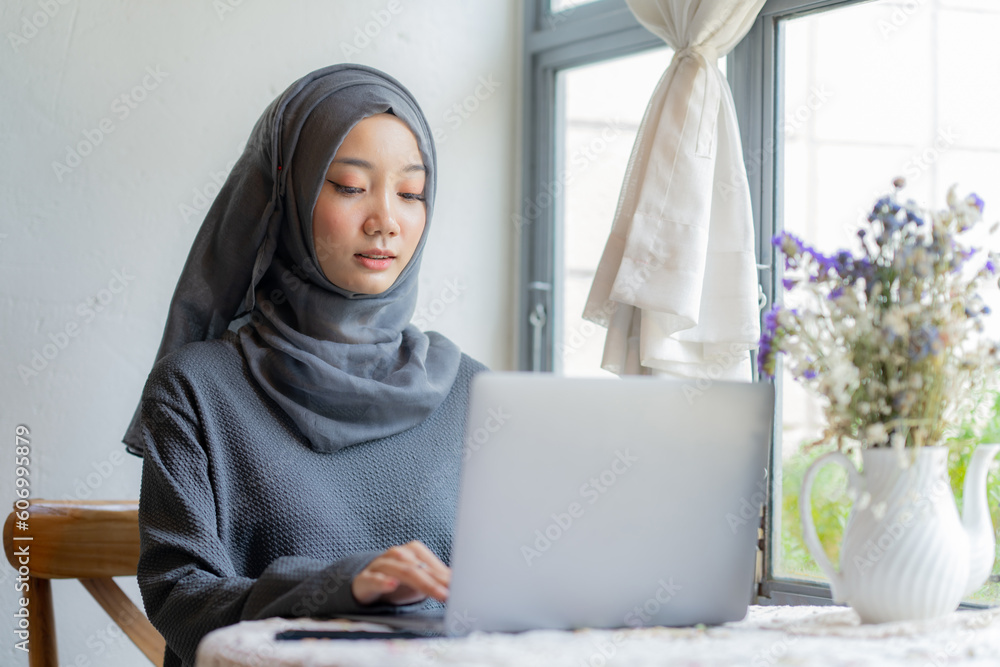 Modern Arab muslim girl in hijab using a laptop computer and mobile phone at home, Cheerful girl sitting at the desk and new order. Successful concept. Modern Arab muslim girl in hijab using a laptop computer and mobile phone at home, Cheerful girl sitting at the desk and new order. Successful concept.