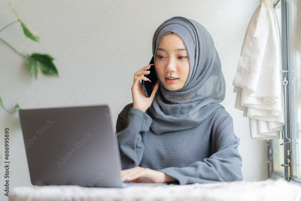 Modern Arab muslim girl in hijab using a laptop computer and mobile phone at home, Cheerful girl sitting at the desk and new order. Successful concept. Modern Arab muslim girl in hijab using a laptop computer and mobile phone at home, Cheerful girl sitting at the desk and new order. Successful concept.