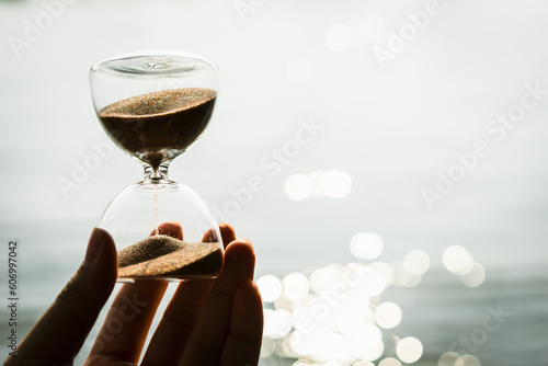 Obraz na plátne Hand holding the hour glass with bokeh of sea background