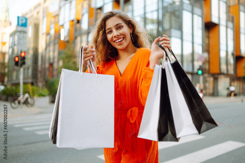 Cheerful young woman with shopping bags walking down the city street. Purchases, black friday, discounts.