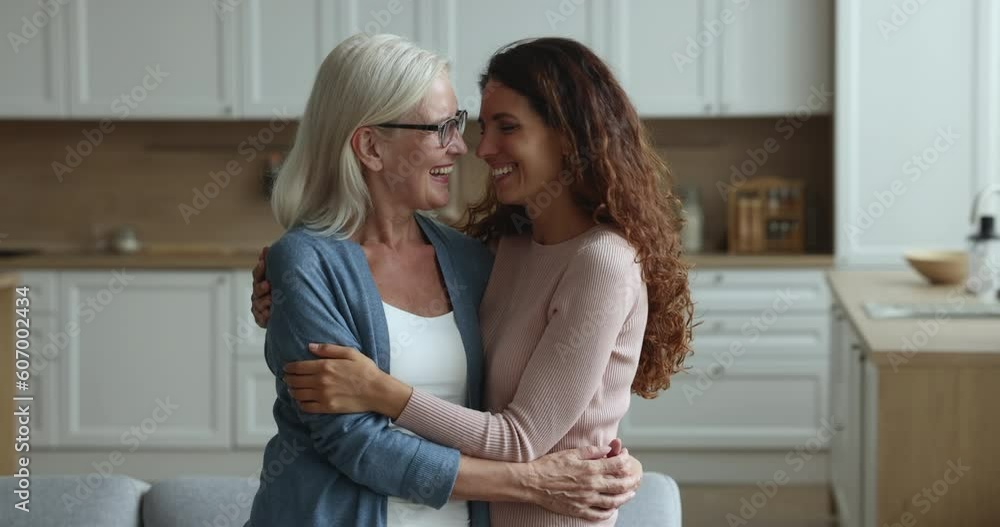Happy elderly retired loving mother and beautiful millennial daughter hugging smiling pose look camera standing together at modern home. Multi-generational family portrait, motherhood, understanding Happy elderly retired loving mother and beautiful millennial daughter hugging smiling pose look camera standing together at modern home. Multi-generational family portrait, motherhood, understanding