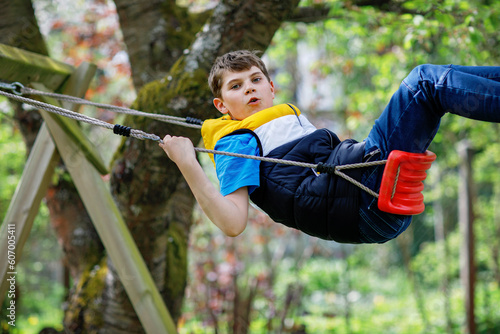 Happy school boy having fun on swing in domestic garden. Healthy child swinging under blooming trees on sunny spring day. Preteen Kid laughing and crying.