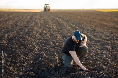Farmer examing dirt while tractor is plowing field