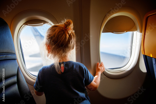 Adorable little girl traveling by an airplane. Child sitting by aircraft window and looking outside. Traveling with kids abroad. Family on summer vacations.