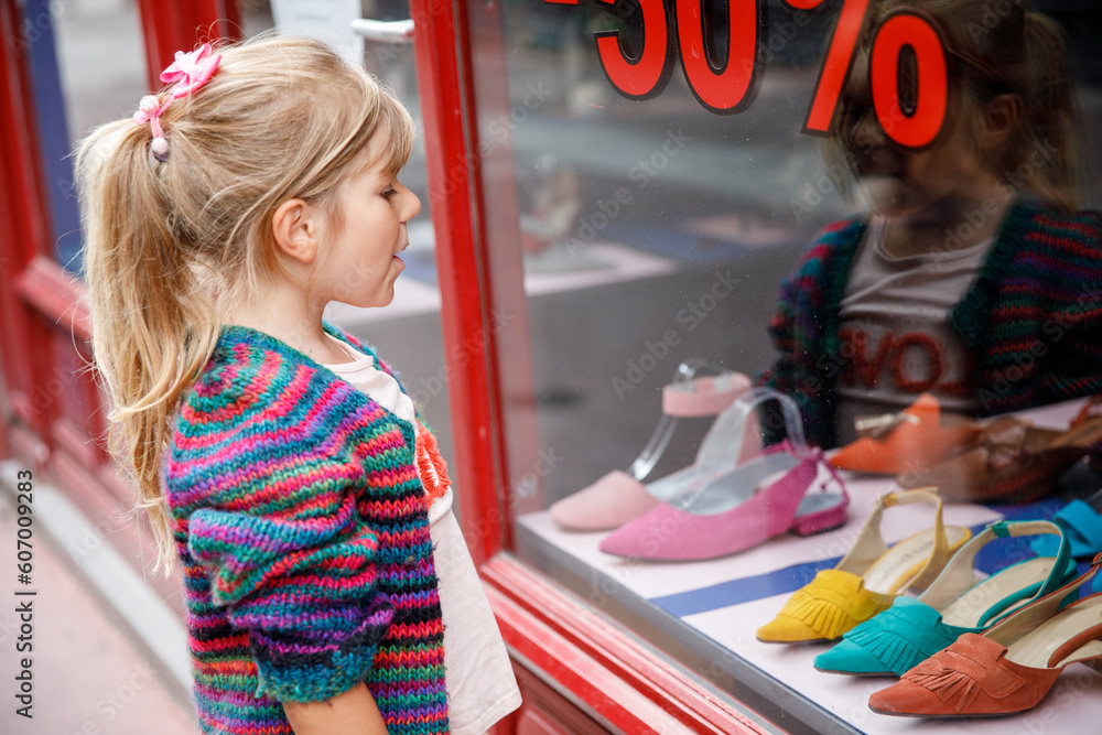 Little Girl looks at the window near the shopping center. Adorable happy child looking on shoes in store window.