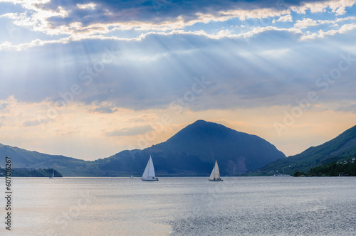 sailboats in sailboats rays of light on the fjord with mountains and clouds