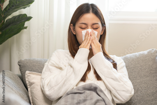 Sick, coronavirus or covid-19, attractive asian young woman, girl have a fever, flu and hand in use tissues paper sneezing nose, runny while sitting on sofa, couch at home. Health care on virus person