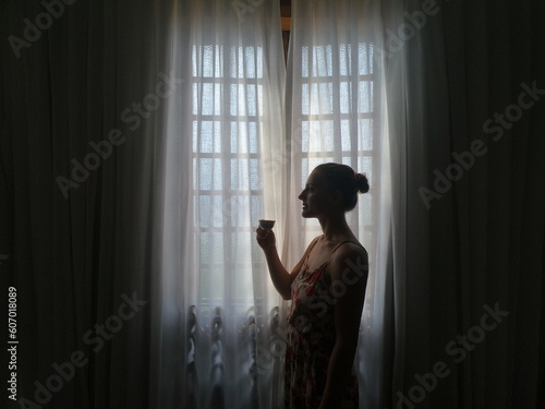 Silhueta de mulher em frente    janela com cortinas 