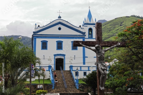 Blue and white Church of Our Lady of Help in Ilhabella, Brazil, with a cross in front of it photo