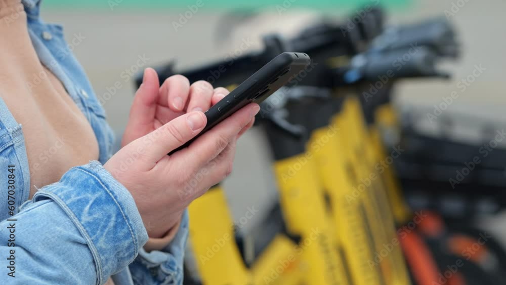 Woman hand scrolls social media on black smartphone. Lady stands in park against bunch of bicycles for tourists and visitors on spring day Woman hand scrolls social media on black smartphone. Lady stands in park against bunch of bicycles for tourists and visitors on spring day
