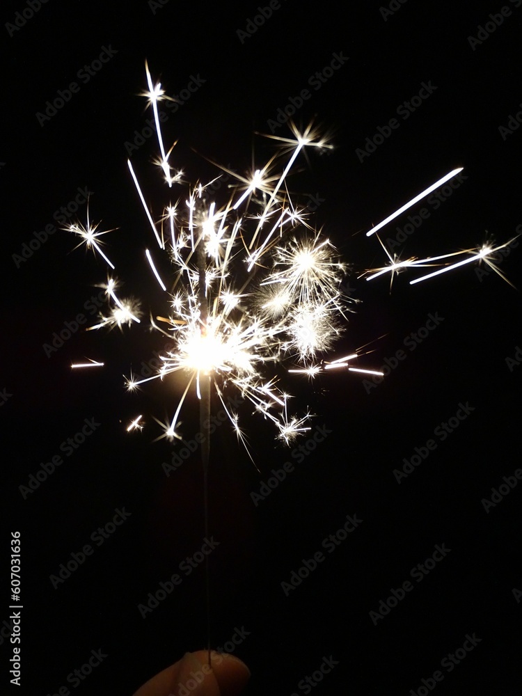 Fototapeta premium Vertical shot of a sparkler in a lady's hand sparkling at night