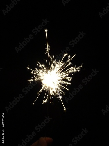 Vertical shot of a sparkler in a lady's hand sparkling at night photo