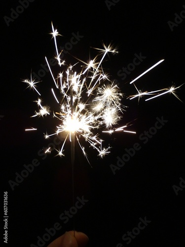 Vertical shot of a sparkler in a lady s hand sparkling at night