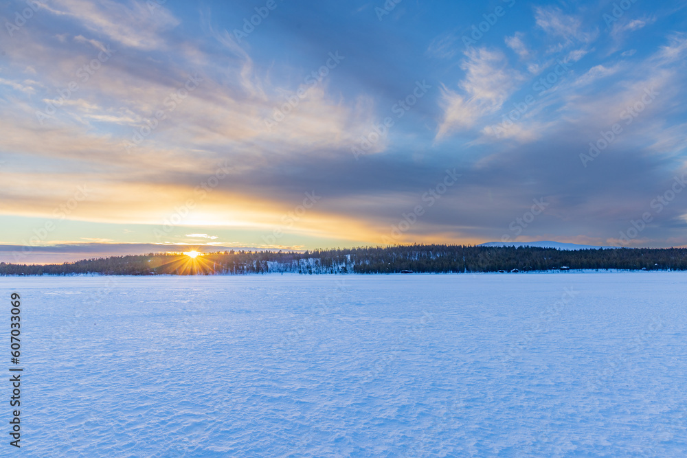 Sunrise over the frozen Ounasjärvi lake with surrounding pine forests and hills in the background in Hetta, Lapland, Finland