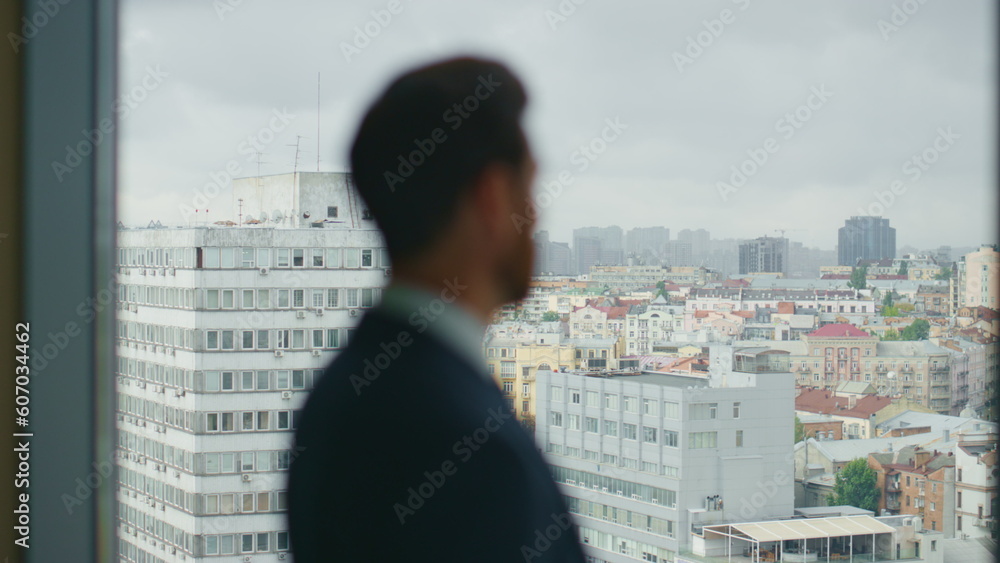 Man standing office window watching at city view close up. Serious businessman. Man standing office window watching at city view close up. Serious businessman.
