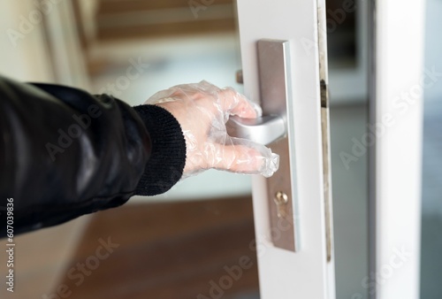 Closeup of human hand wearing disposable plastic gloves and touching doors knob