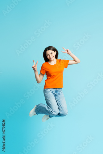 Portrait of smiling cheerful teenage girl jumping gesturing isolated on blue background