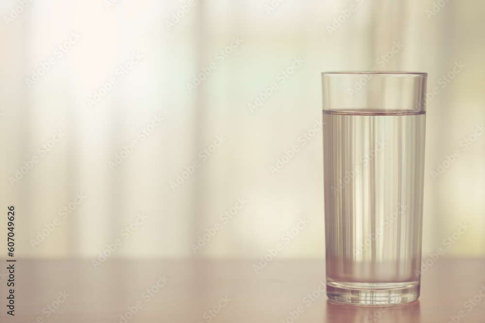 Glass of drinking water on blurred white curtain background with sun light effect for healthy drinking and beverages concept Glass of drinking water on blurred white curtain background with sun light effect for healthy drinking and beverages concept
