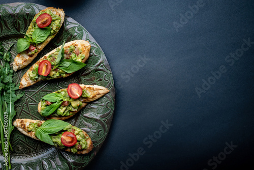 Bruschettas french toasts with guacamole, basil and cherry tomatoes served on beautiful plate with arugula. Antipasti with slice bread, mashed avocado and vegetables on background with copy space