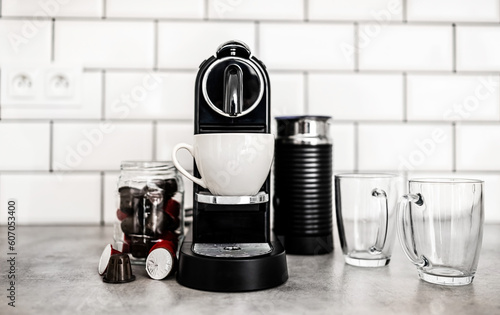 Coffee machine with different capsules and transparent cups at domestic kitchen at home. Espresso caffeine beverage maker and modern mugs