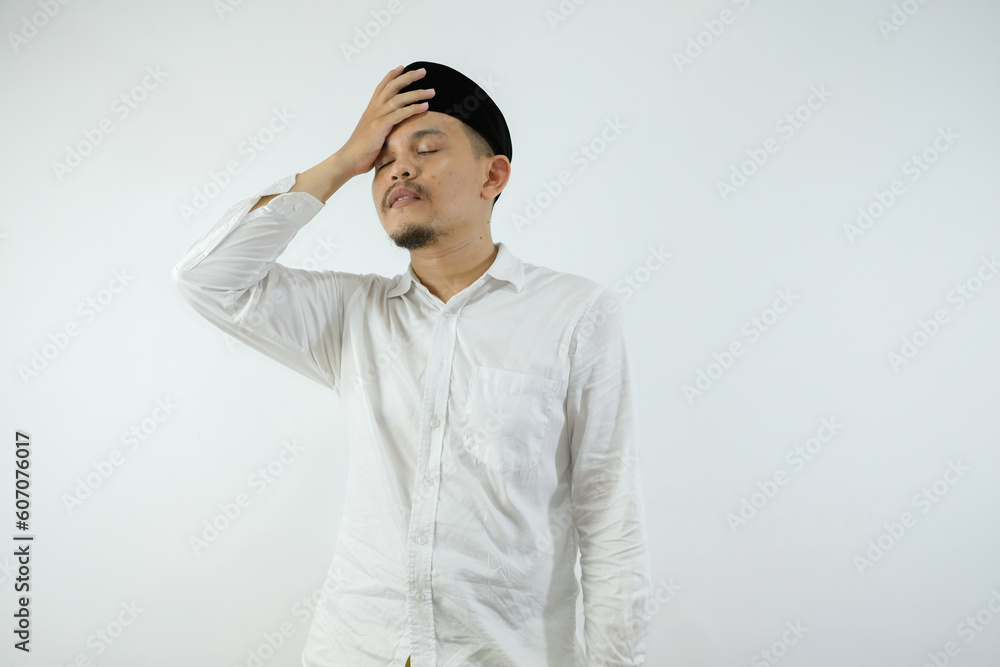 Stressed Asian Muslim man in white clothes and black skull cap touching his temples and having headache isolated over white background Stressed Asian Muslim man in white clothes and black skull cap touching his temples and having headache isolated over white background