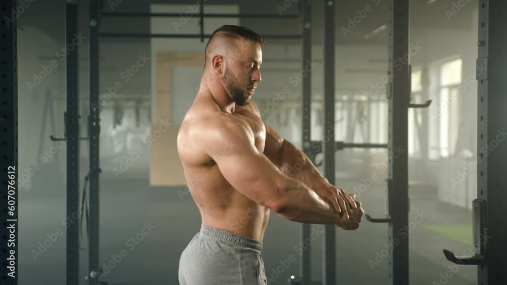 Profile shot of middle-aged sportsman showing his bare muscular torso, biceps and triceps. Man poses in gym standing on the background of power rack. High quality 4k footage Profile shot of middle-aged sportsman showing his bare muscular torso, biceps and triceps. Man poses in gym standing on the background of power rack. High quality 4k footage