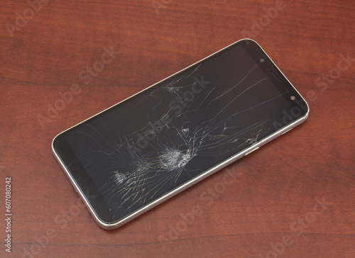 Mobile phone with broken screen on wooden table.