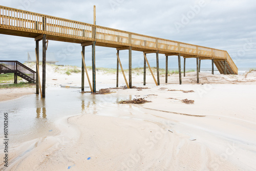 Elevated wooden boardwalk over grassy beach sand dunes next to the waves of the surf under a cloudy sky