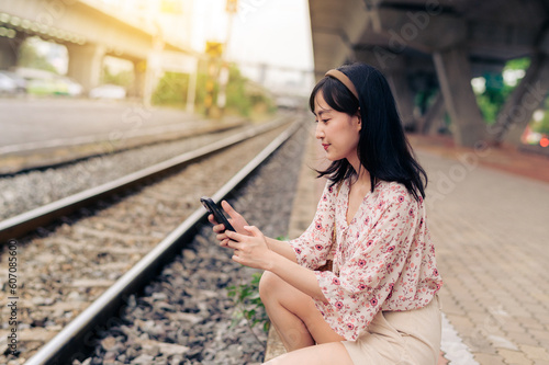 Asian young woman traveler with weaving basket using a mobile phone beside railway train station in Bangkok. Journey trip lifestyle, world travel explorer or Asia summer tourism concept. © Jirawatfoto