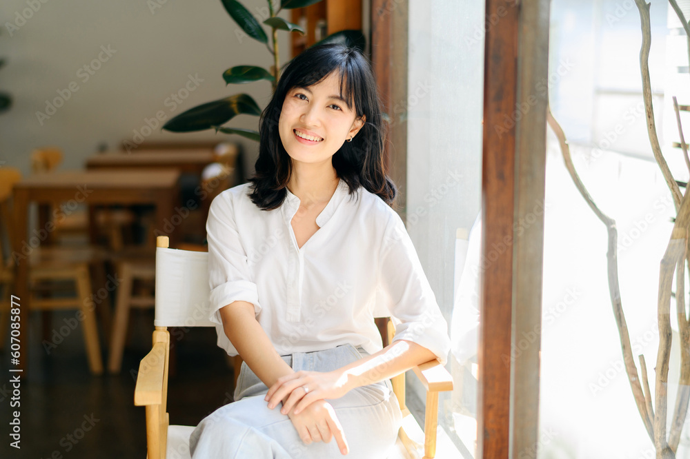 Brightly smiling beautiful young asian woman sitting in coffee cafe in sunny day Brightly smiling beautiful young asian woman sitting in coffee cafe in sunny day