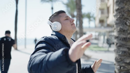 Young hispanic man listening to music and dancing at street