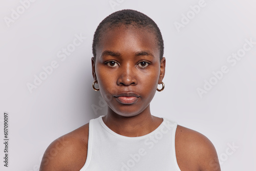 Portrait of young A American woman confidently looks at camera stands indoor dressed in comfortable tshirt has simple expression reveals depth of thought and contemplation poses over white background © Wayhome Studio