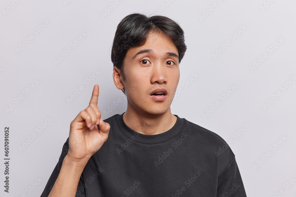 Shocked Japanese man finds solutio being stroke with amazing idea keeps index finger raised up in eureka gesture dressed in casual black t shirt isolated over white backgroun has suggestion or plan Shocked Japanese man finds solutio being stroke with amazing idea keeps index finger raised up in eureka gesture dressed in casual black t shirt isolated over white backgroun has suggestion or plan