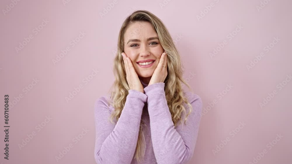 Young blonde woman smiling confident touching face with hands over isolated pink background Young blonde woman smiling confident touching face with hands over isolated pink background
