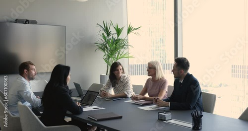 Confident senior elder businesswoman talking to team of colleagues, partners on meeting. Corporate teacher discussing educating tasks with mentors. Diverse team brainstorming at table